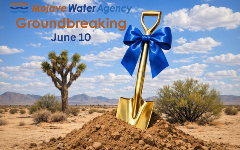 A gold shovel with a blue bow stands in a dirt mound in a desert landscape, with text announcing the Mojave Water Agency Groundbreaking on June 10.